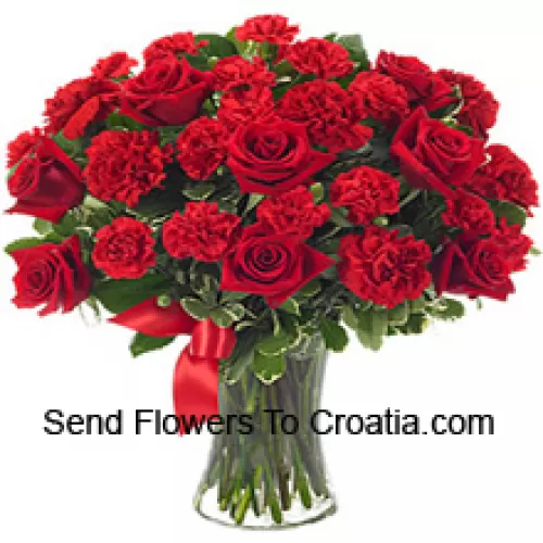 15 roses rouges et 10 oeillets rouges avec quelques fougères dans un vase en verre